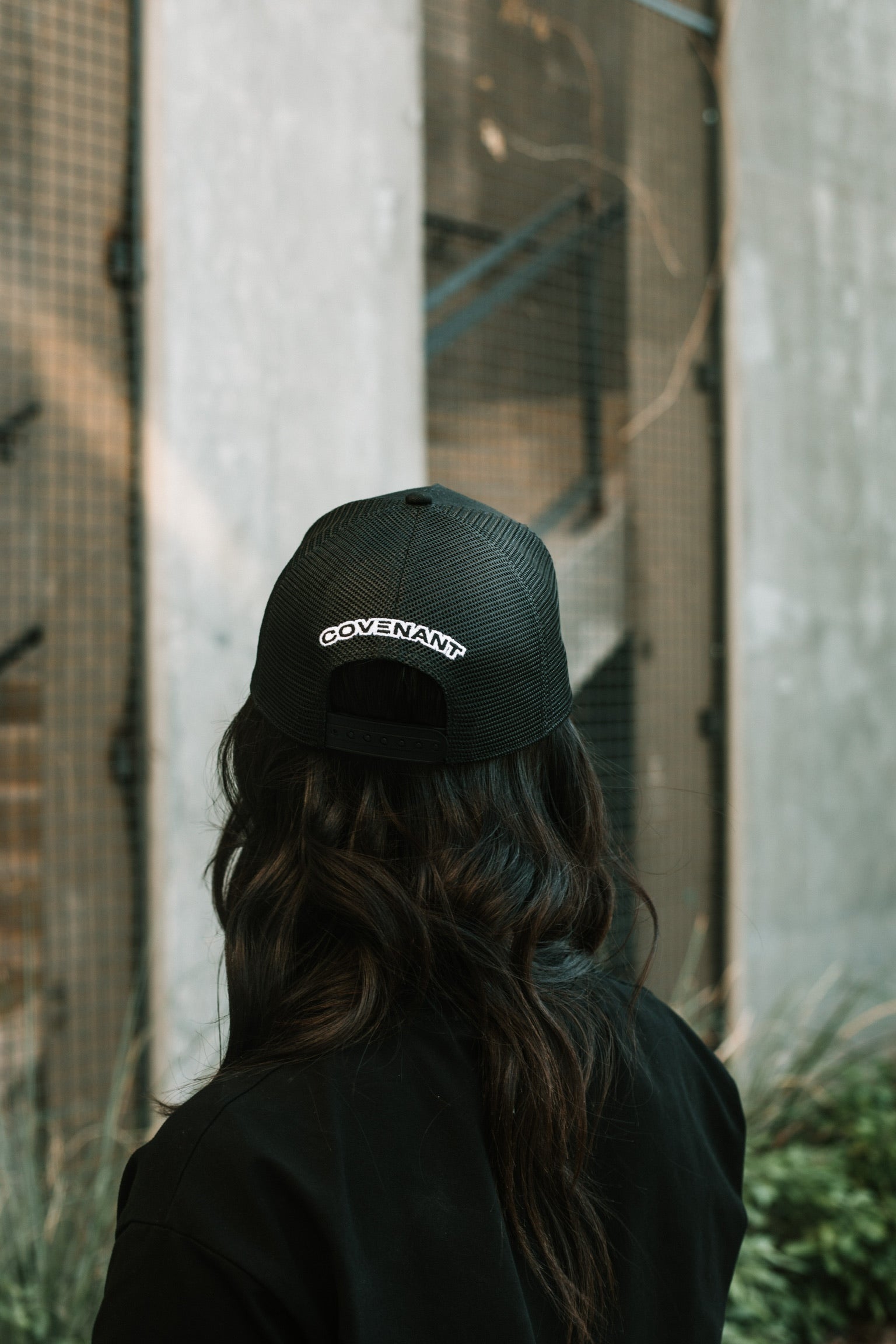 Female model showing the back of the Original Trucker Hat with the "Covenant" logo above the snap back.